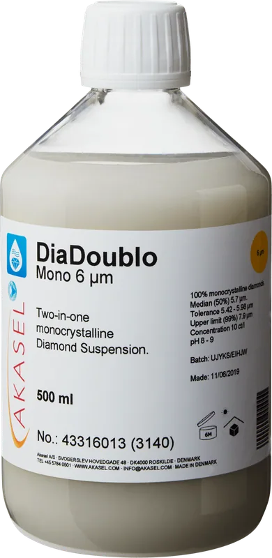 Akasel DiaDoublo Mono 6 µm: En 500 ml plastflaska med vit skruvkork, innehållande en ljus, mjölkvit monokristallin diamantsuspension. Etiketten visar produktnamnet “DiaDoublo Mono 6 µm” tillsammans med beskrivningen “Two-in-one monocrystalline Diamond Suspension.” Ytterligare detaljer inkluderar: “100% monocrystalline diamonds,” “Median (50%) 5.7 µm,” “Tolerance 5.42 – 5.98 µm,” “Upper limit (99%) 7.9 µm,” och en koncentration på “10 ct/l.” Symboler på etiketten anger lagringsförhållanden och hållbarhet.
